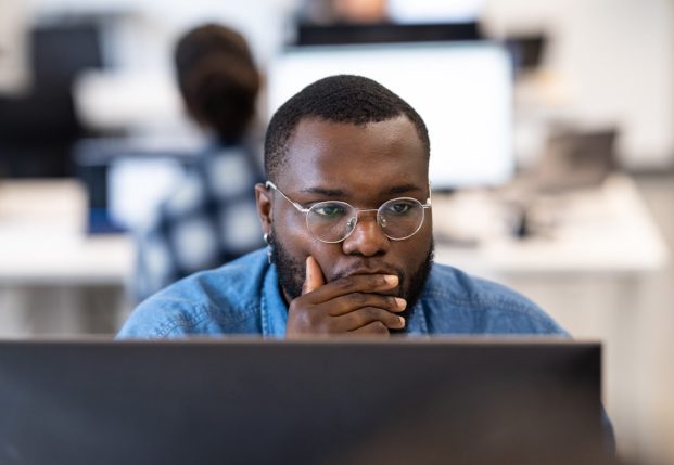 Developer with glasses looking at computer with hand over mouth concentrating on information on the screen. Developer with glasses looking at computer with hand over mouth concentrating on information on the screen.