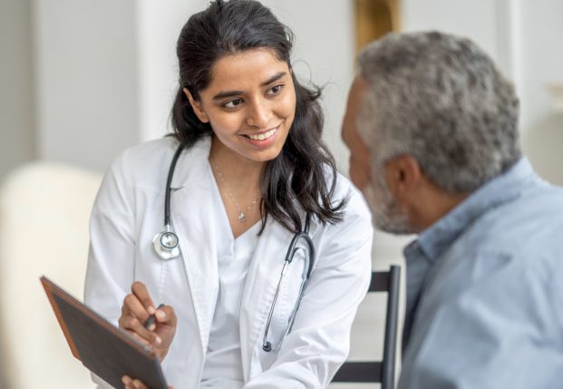Doctor sitting with patient holding a clipboard while smiling Doctor sitting with patient holding a clipboard while smiling