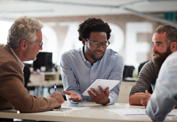 People in office working together review information on a tablet in a conference room. People in office working together review information on a tablet in a conference room.