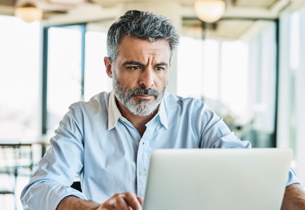 Older person in buttoned up shirt at home working on computer. Older person in buttoned up shirt at home working on computer.