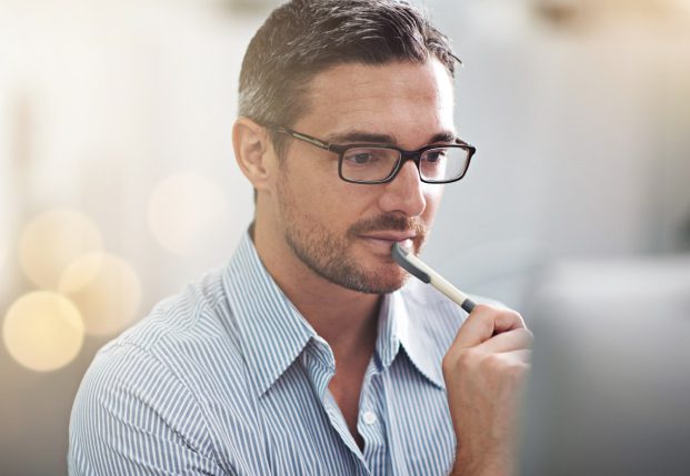 Clean cut business man with glasses holding a pen looking at a computer screen. Clean cut business man with glasses holding a pen looking at a computer screen.